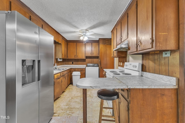 kitchen with brown cabinetry, washer / dryer, under cabinet range hood, stainless steel fridge, and white range with electric stovetop