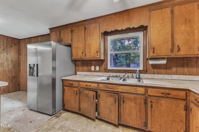 kitchen featuring stainless steel fridge, light countertops, wood walls, and a sink