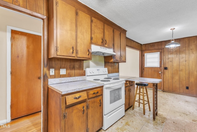 kitchen featuring wooden walls, under cabinet range hood, light countertops, white electric range oven, and brown cabinetry