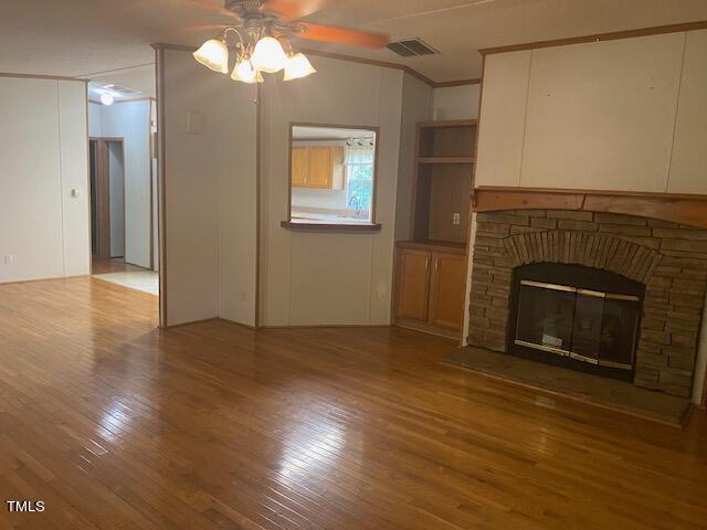 unfurnished living room featuring ceiling fan, hardwood / wood-style flooring, a fireplace, and ornamental molding