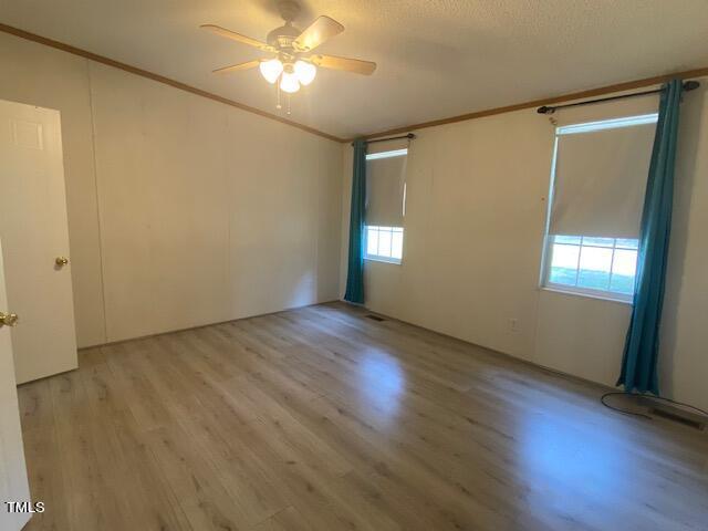 empty room with ceiling fan, crown molding, wood-type flooring, and a textured ceiling