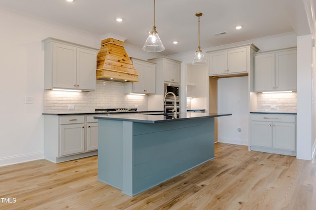 kitchen with dark countertops, premium range hood, ornamental molding, light wood-style floors, and a sink