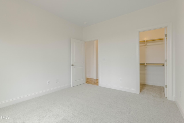 unfurnished bedroom featuring a walk in closet, baseboards, a closet, and carpet flooring