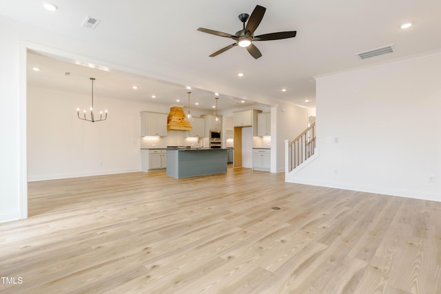 unfurnished living room with light wood finished floors, visible vents, baseboards, stairway, and ceiling fan with notable chandelier