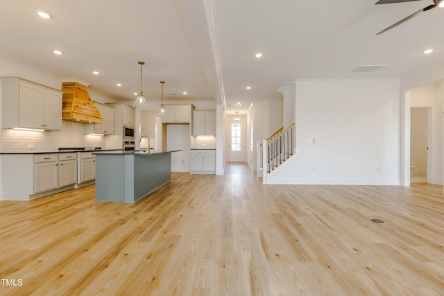 kitchen featuring dark countertops, light wood-type flooring, custom range hood, ornamental molding, and a sink