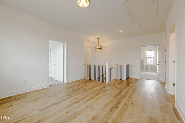 unfurnished room with attic access, baseboards, and light wood finished floors