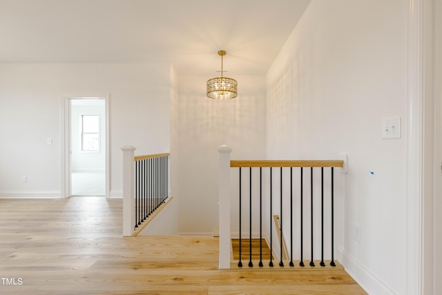 hallway featuring wood finished floors, an upstairs landing, baseboards, and a chandelier