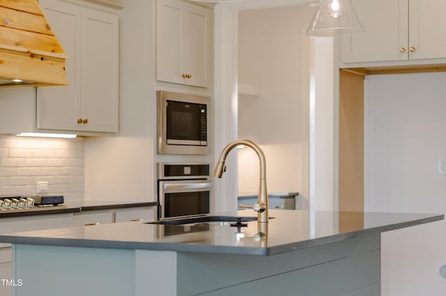 kitchen featuring a sink, tasteful backsplash, white cabinets, built in microwave, and custom exhaust hood