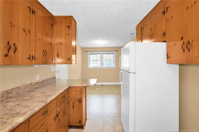 kitchen featuring white refrigerator, a textured ceiling, and kitchen peninsula