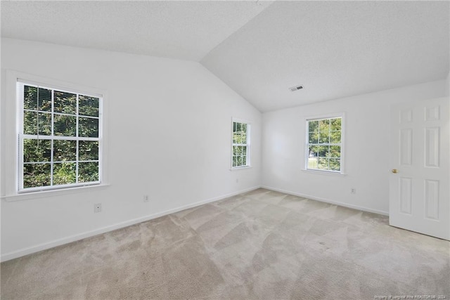 spare room featuring a textured ceiling, light colored carpet, and vaulted ceiling