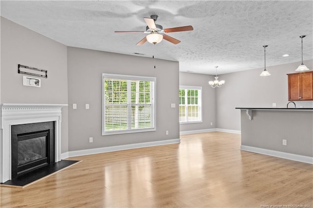 unfurnished living room with ceiling fan with notable chandelier, a textured ceiling, and light hardwood / wood-style flooring