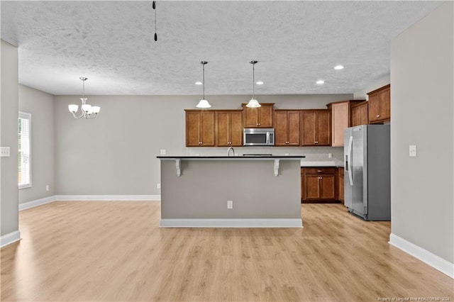 kitchen featuring a center island with sink, hanging light fixtures, stainless steel appliances, a breakfast bar, and light wood-type flooring