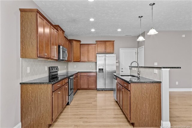 kitchen with dark stone countertops, light hardwood / wood-style flooring, appliances with stainless steel finishes, sink, and pendant lighting