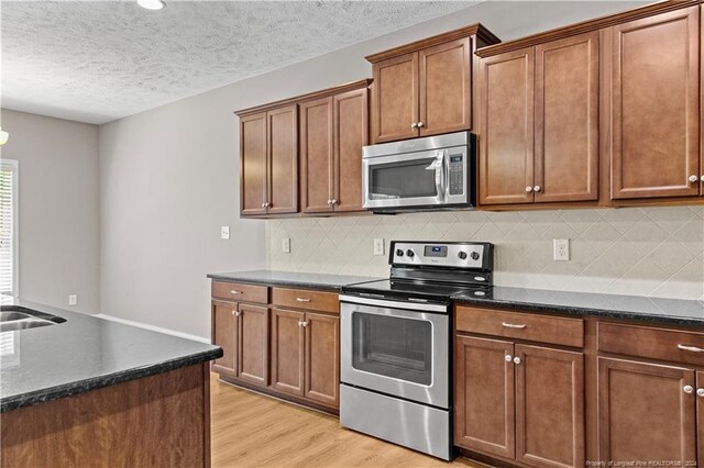 kitchen with a textured ceiling, light hardwood / wood-style flooring, backsplash, and stainless steel appliances