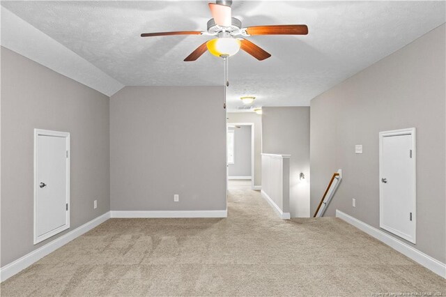 carpeted spare room with ceiling fan, a textured ceiling, and vaulted ceiling