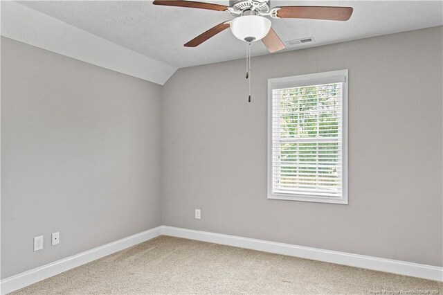 empty room featuring lofted ceiling, ceiling fan, carpet floors, and a textured ceiling