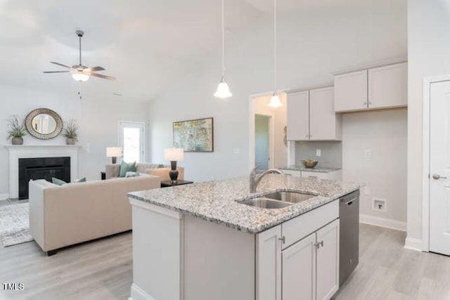 kitchen featuring light stone counters, white cabinetry, light wood-type flooring, sink, and an island with sink