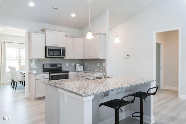 kitchen featuring white cabinetry, light wood-type flooring, stainless steel appliances, and hanging light fixtures