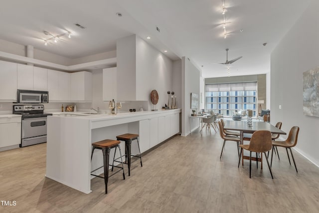 kitchen with appliances with stainless steel finishes, a breakfast bar, kitchen peninsula, white cabinetry, and ceiling fan