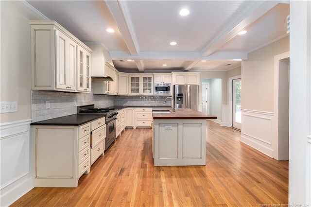 kitchen with stainless steel appliances, a center island with sink, decorative backsplash, and beam ceiling