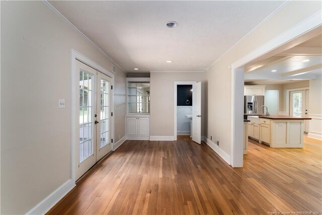 doorway with a healthy amount of sunlight, ornamental molding, light wood-type flooring, and french doors