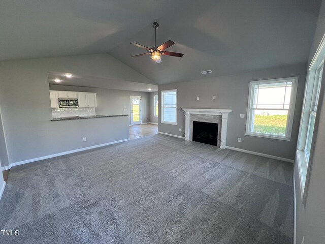 unfurnished living room featuring plenty of natural light, ceiling fan, a premium fireplace, and vaulted ceiling