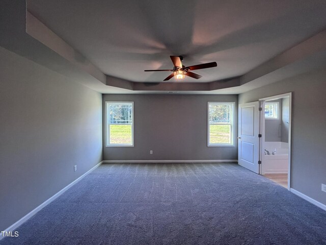 empty room with a tray ceiling, a healthy amount of sunlight, ceiling fan, and carpet flooring