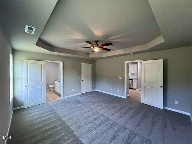 unfurnished bedroom featuring carpet, ceiling fan, connected bathroom, and a raised ceiling