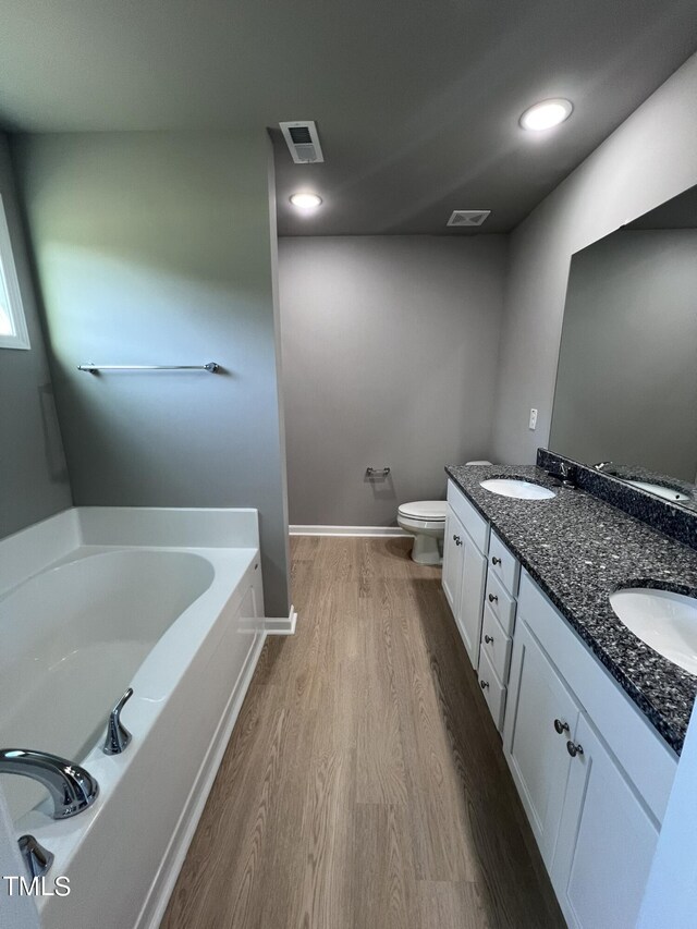 bathroom with a tub to relax in, toilet, wood-type flooring, and vanity