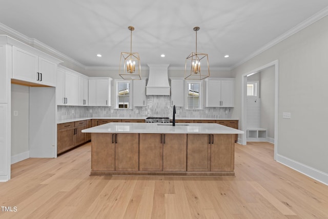 kitchen featuring light hardwood / wood-style floors, white cabinetry, pendant lighting, custom exhaust hood, and a center island with sink