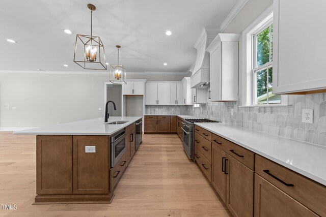 kitchen featuring an island with sink, sink, decorative light fixtures, white cabinetry, and stainless steel appliances