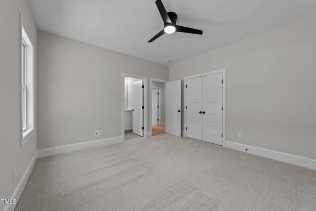 unfurnished bedroom featuring ceiling fan, a closet, connected bathroom, and light carpet