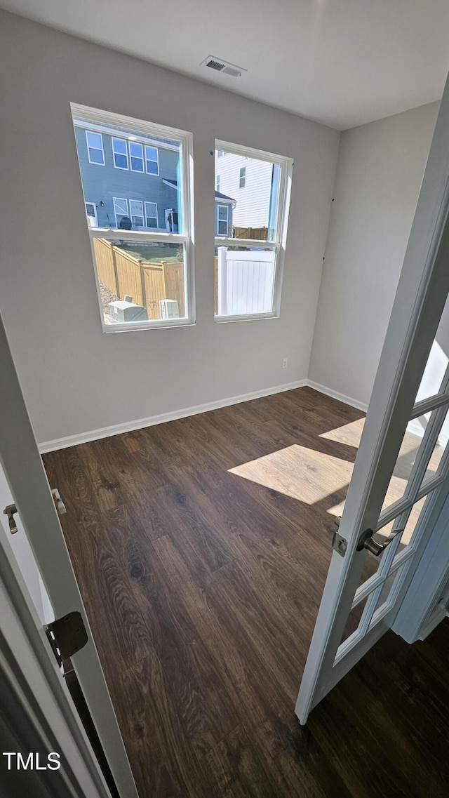 unfurnished room with baseboards, visible vents, and dark wood finished floors