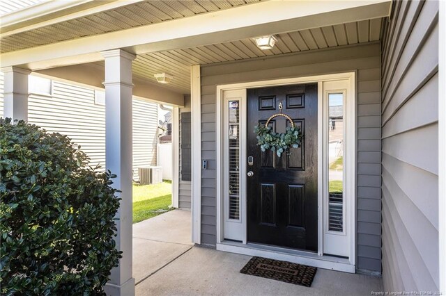 view of exterior entry featuring covered porch and cooling unit