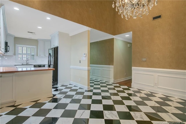 interior space with white cabinets, crown molding, black fridge, and decorative backsplash