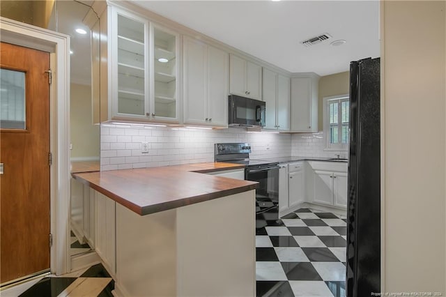 kitchen featuring kitchen peninsula, tasteful backsplash, white cabinetry, black appliances, and butcher block counters