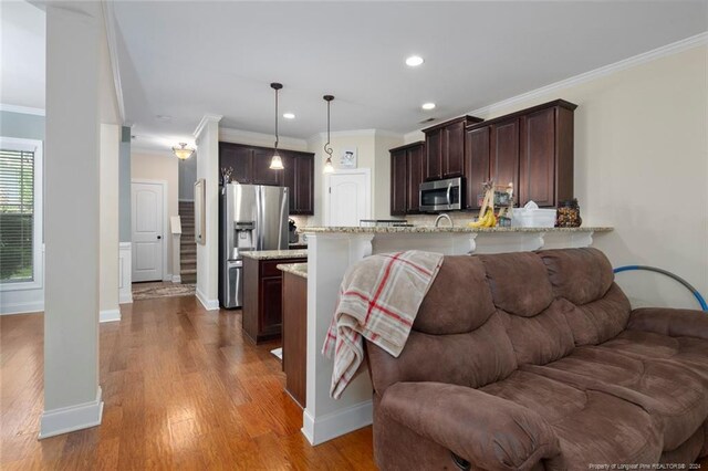 kitchen featuring light wood-type flooring, appliances with stainless steel finishes, kitchen peninsula, and light stone countertops