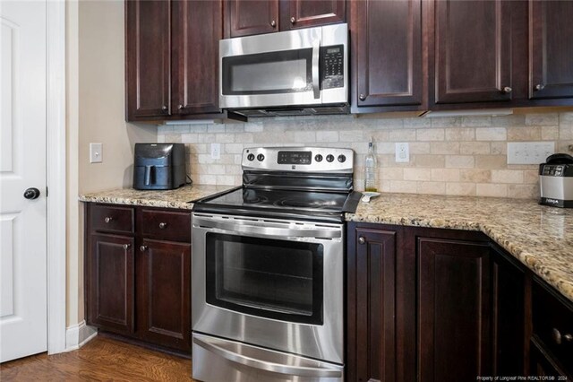 kitchen featuring wood-type flooring, light stone counters, appliances with stainless steel finishes, and tasteful backsplash