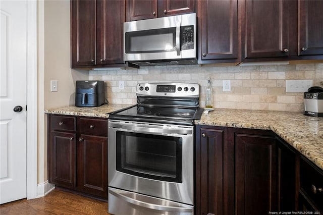 kitchen with light stone countertops, stainless steel appliances, dark brown cabinets, dark wood-style floors, and backsplash
