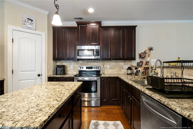 kitchen featuring decorative light fixtures, light stone countertops, dark hardwood / wood-style flooring, appliances with stainless steel finishes, and ornamental molding