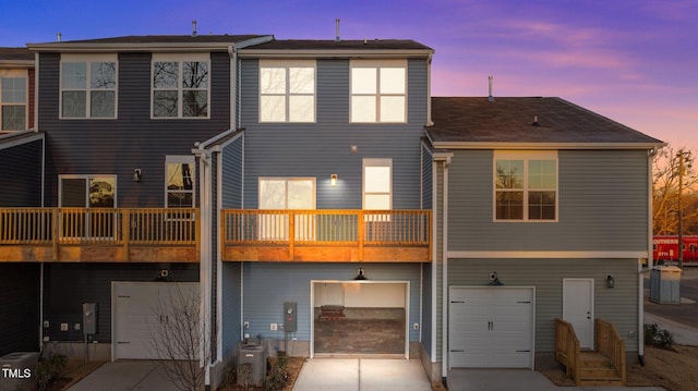 back house at dusk with a balcony, a garage, and cooling unit