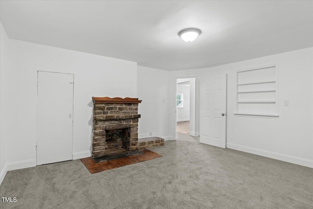 unfurnished living room with built in features, a stone fireplace, and carpet floors