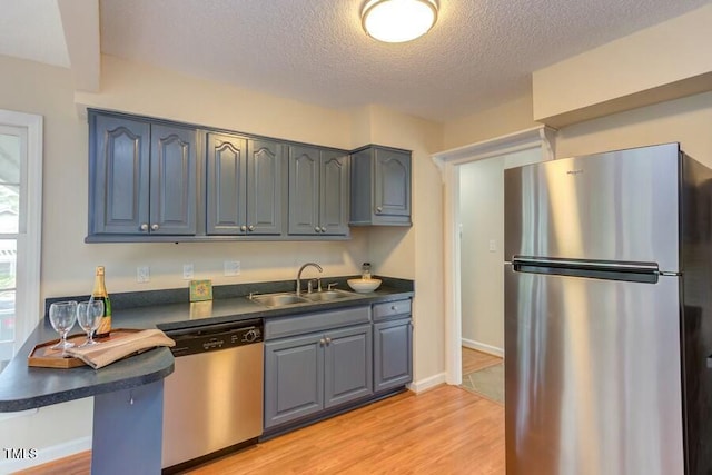 kitchen featuring dark countertops, light wood finished floors, gray cabinets, appliances with stainless steel finishes, and a sink