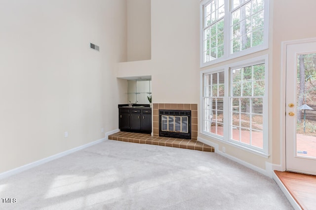 unfurnished living room featuring carpet, visible vents, baseboards, a high ceiling, and plenty of natural light