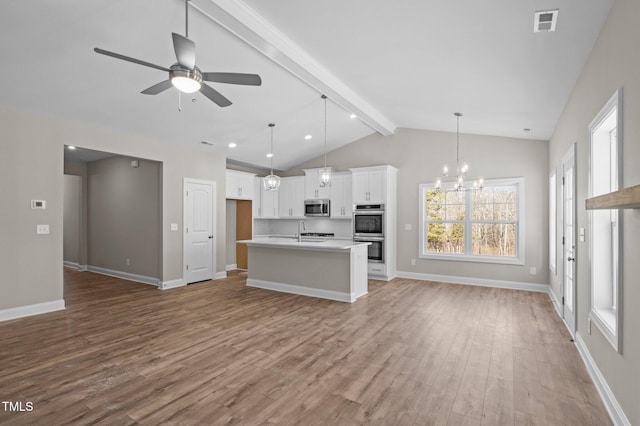 kitchen featuring pendant lighting, appliances with stainless steel finishes, white cabinetry, hardwood / wood-style floors, and an island with sink