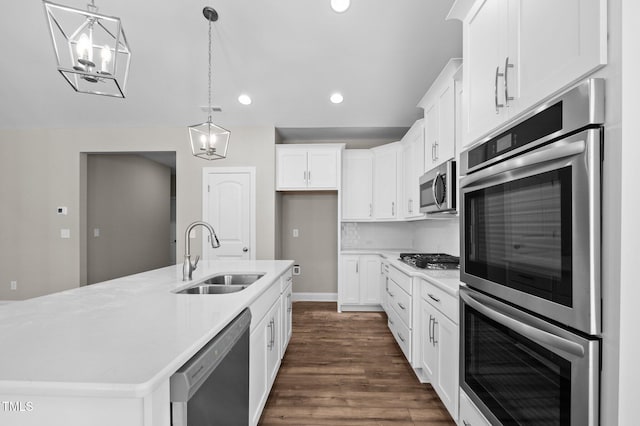 kitchen with sink, hanging light fixtures, stainless steel appliances, a kitchen island with sink, and white cabinets