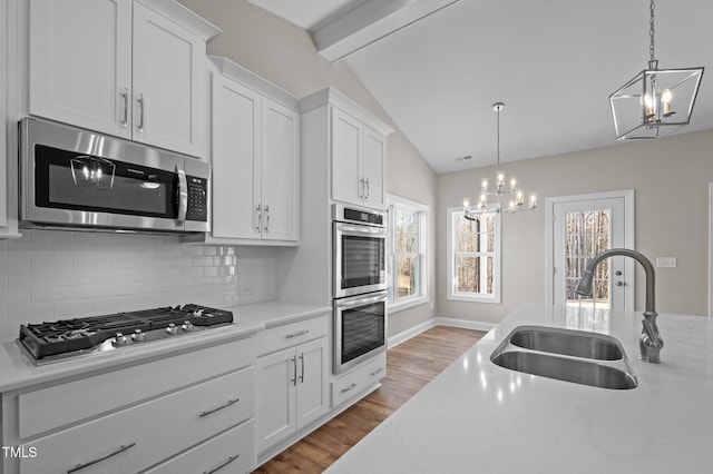 kitchen with sink, white cabinetry, vaulted ceiling with beams, stainless steel appliances, and decorative light fixtures