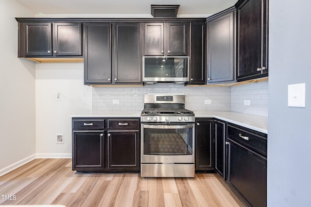 kitchen with light wood finished floors, appliances with stainless steel finishes, light countertops, and backsplash