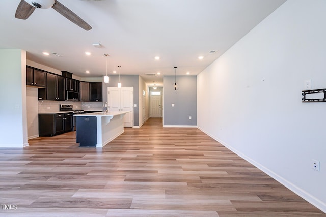 kitchen featuring a center island with sink, baseboards, open floor plan, stainless steel appliances, and backsplash