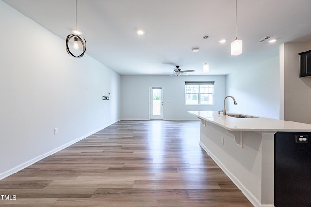 kitchen with a center island with sink, light countertops, visible vents, a sink, and light wood-type flooring